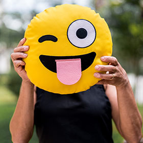 Mulher com almofada de emoji mostrando<br />a língua