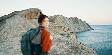 Woman in a red sweater in the mountains on nature and a backpack on her back blue sea sky autumn