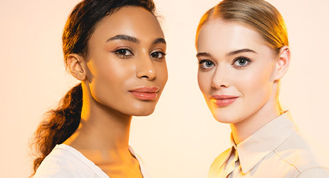 Two attractive multicultural women with makeup looking at camera isolated on beige — Stock Photo #338575566