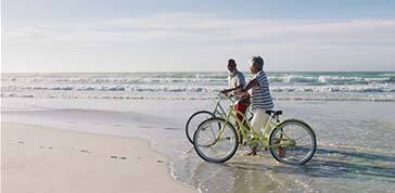 Senior african american couple walking with bicycles at the beach. healthy outdoor leisure time by the sea.