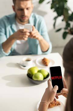 KYIV, UKRAINE - FEBRUARY 21, 2020: Selective focus of woman using smartphone with netflix app near boyfriend and breakfast on table